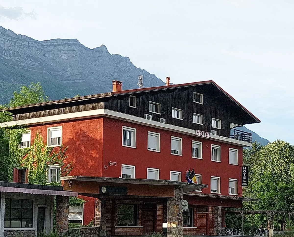 Façade rouge de l’hôtel Ô & Cimes avec les montagnes en arrière-plan